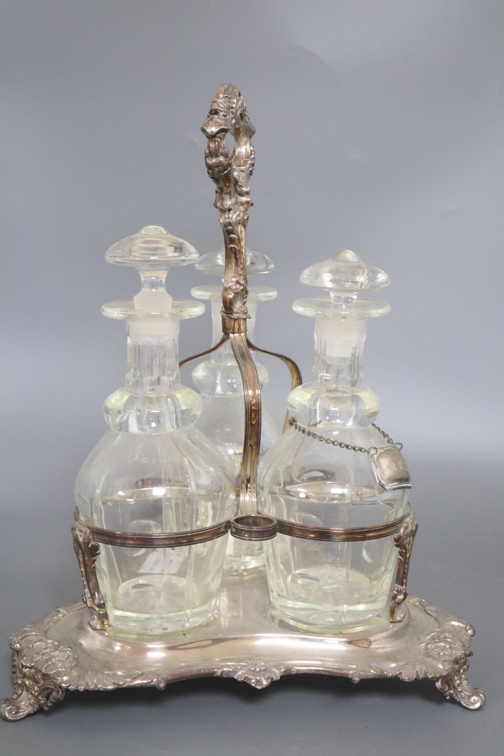 A plated three decanter tantalus of triangular form with leaf-wrapped handle, with bottles and stoppers, height 38cm